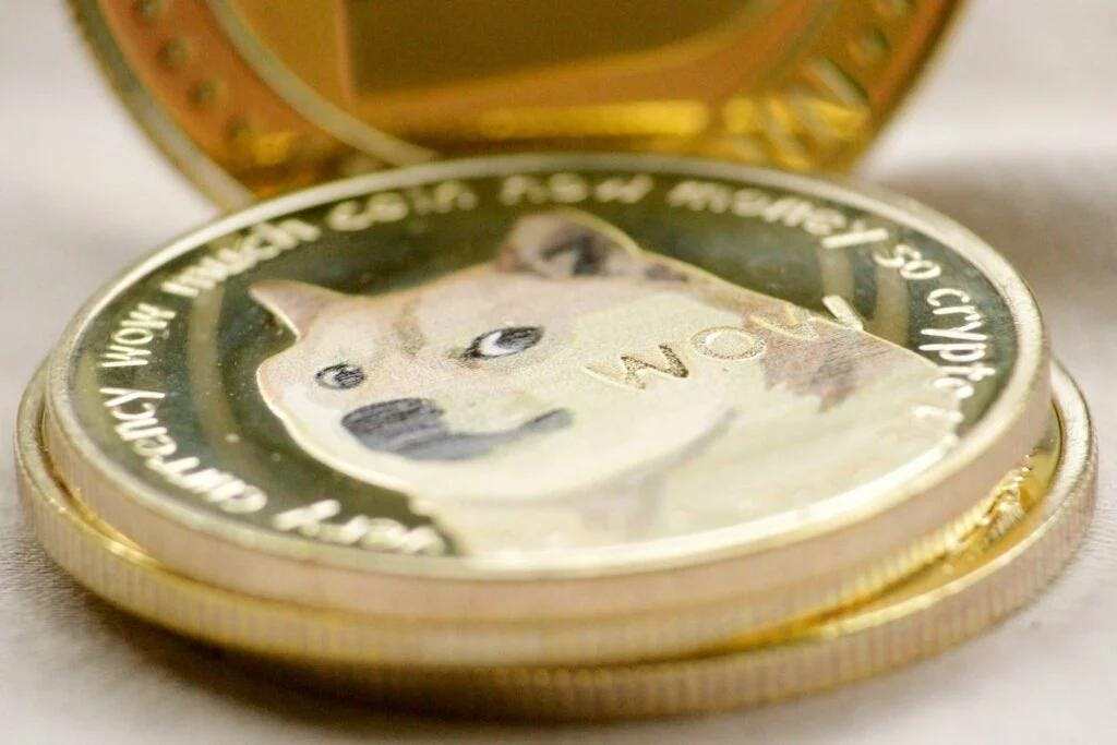 A close-up image of a physical Dogecoin, featuring the famous Shiba Inu dog from the 'Doge' meme. The coin has the dog's face in the center, with the word 'WOW' prominently displayed. The text around the edge of the coin reads phrases like 'Currency' and 'Wow much coin how money so crypto.'